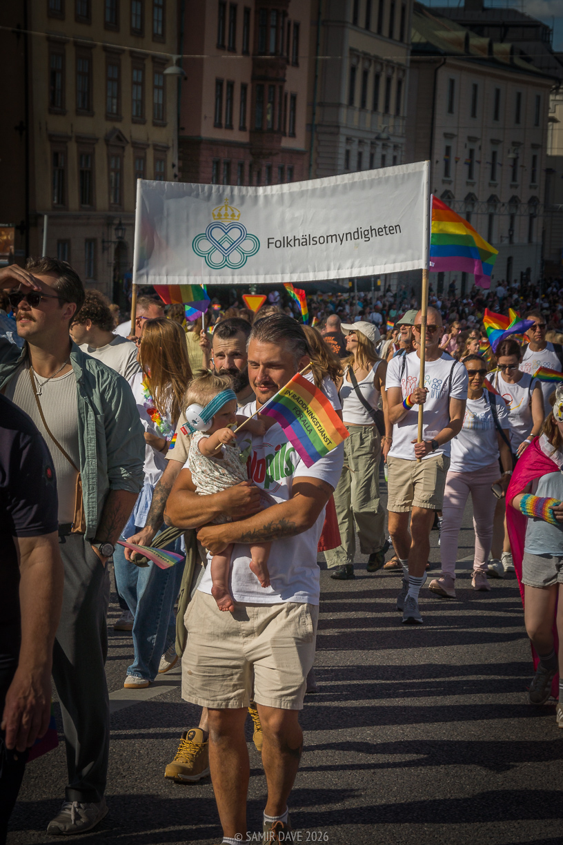 A member from the Swedish public health agency aka Folkhälsomyndigheten carrying a child waving the pride flag at Stockholm Pride Festival 2026.